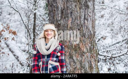 donna sorridente vicino all'albero. festa invernale giorno. donna carina in abiti caldi. Godersi la natura wintertime. Ritratto di donna eccitata in inverno. Ragazza allegra all'aperto relax. Giacca a scacchi donna. Foto Stock