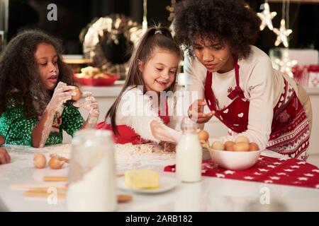 Due ragazze che fanno i biscotti con la mamma a Natale Foto Stock