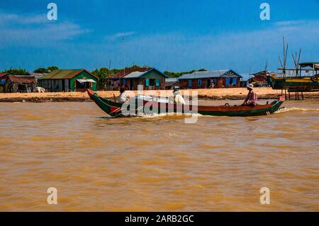 Una lunga barca passando da capanne sulla riva sabbiosa del lago Tonle Sap, in Cambogia. Foto Stock