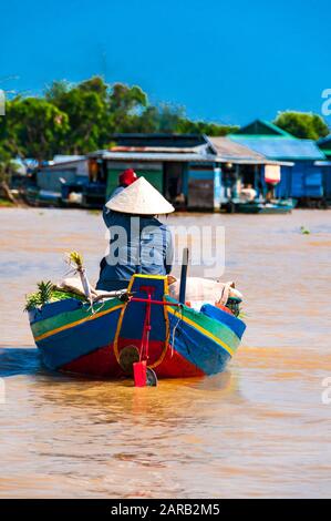 Una donna righe una colorata blu, rosso, verde e giallo barca con una fornitura di frutta e verdura in Chong Kneas, Lago Tonle Sap, in Cambogia. Foto Stock