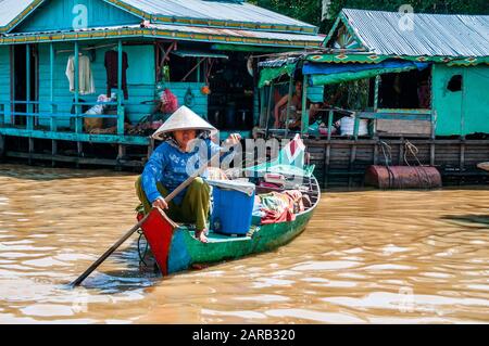 Una donna di canottaggio una colorata barca da alcune case galleggianti a Chong Kneas villaggio sul lago Tonle Sap, in Cambogia. Foto Stock