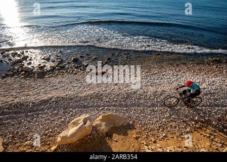 Mountain biker che si muove in spiaggia costiera; El Charco Beach; Villajoyosa villaggio; provincia di Alicante; Spagna Foto Stock