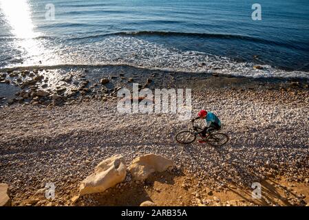 Mountain biker che si muove in spiaggia costiera; El Charco Beach; Villajoyosa villaggio; provincia di Alicante; Spagna Foto Stock