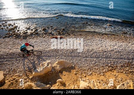 Mountain biker che si muove in spiaggia costiera; El Charco Beach; Villajoyosa villaggio; provincia di Alicante; Spagna Foto Stock