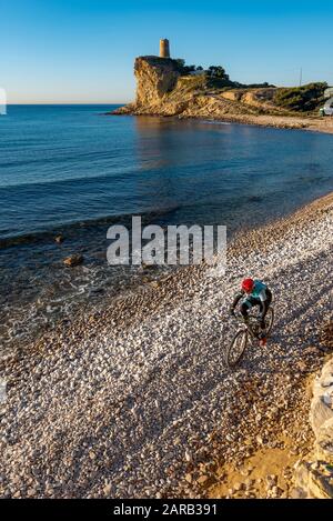 Mountain biker che si muove in spiaggia costiera; El Charco Beach; Villajoyosa villaggio; provincia di Alicante; Spagna Foto Stock