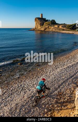 Mountain biker che si muove in spiaggia costiera; El Charco Beach; Villajoyosa villaggio; provincia di Alicante; Spagna Foto Stock