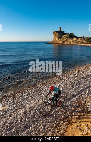 Mountain biker che si muove in spiaggia costiera; El Charco Beach; Villajoyosa villaggio; provincia di Alicante; Spagna Foto Stock