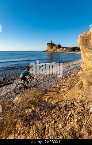 Mountain biker che si muove in spiaggia costiera; El Charco Beach; Villajoyosa villaggio; provincia di Alicante; Spagna Foto Stock