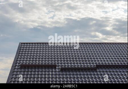 Pendenza del tetto coperta da lastre metalliche effetto piastrelle di colore marrone scuro. Foto Stock