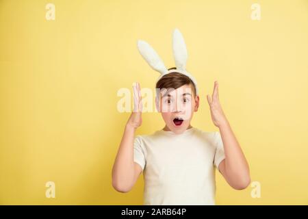 Scioccato, stupito, chiesto. Ragazzo caucasico come coniglietto pasquale su sfondo giallo. Auguri di buona pasqua. Bel modello maschile. Concetto di emozioni umane, espressione facciale, vacanze. Copyspace. Foto Stock