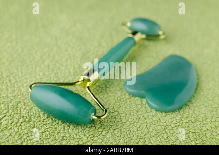 real jade rullo viso e massaggio pietra gua sha su sfondo verde, closeup Foto Stock