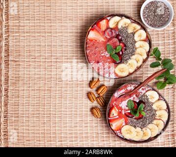 colazione sana. ciotola per frullati con fragole, ciliegie, semi di chia su sfondo di cemento paglia. vista dall'alto. copia spazio Foto Stock