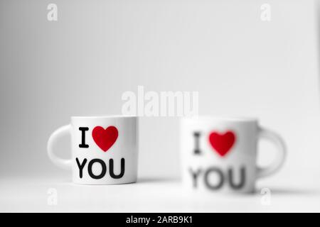 Due coppe bianche con un cuore rosso e un'iscrizione vi amo su sfondo bianco Foto Stock
