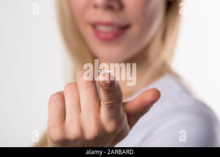 La lente a contatto morbida si trova sul dito della mano femmina su uno sfondo bianco Foto Stock