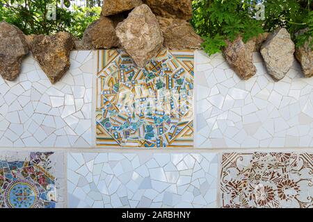 Dettagli del mosaico del trencadis della parete in ceramica e pietra del Parco Guell progettato da Antoni Gaudi, Barcellona, Spagna. Foto Stock