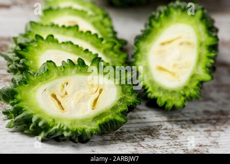 Primo piano di alcune fette di materie karela, noto anche come il melone amaro o bitter gourd, su un bianco tavola in legno rustico Foto Stock