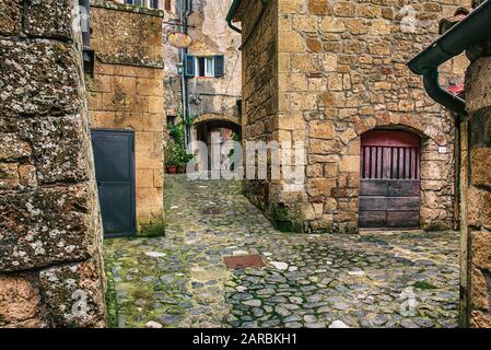 Stradina medievale di antica città di tufo Sorano con piante verdi e ciottoli, viaggiare in Italia lo sfondo Foto Stock