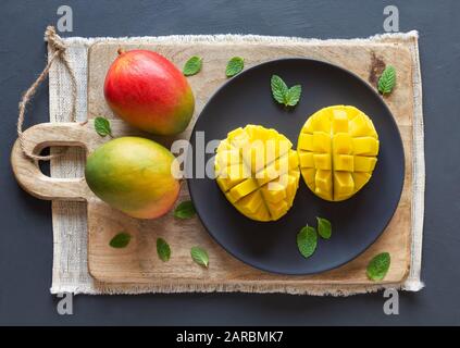 Mango tagliato a metà e cubato su una tavola di legno, due mango intero, sfondo rustico, vista dall'alto Foto Stock