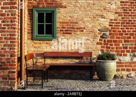 Banco vuoto in mattoni angolo muro con finestra piccola. Fotografia di stili vintage. Luogo invitante a riposo. Foto Stock