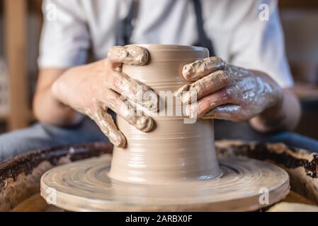 Potter che lavora su una ruota di Potter che fa un vaso. Giovane donna che forma l'argilla con le mani creando brocca in un laboratorio. Primo piano Foto Stock