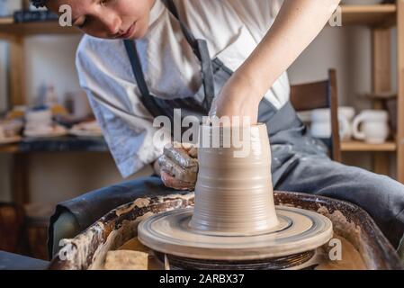 Potter che lavora su una ruota di Potter che fa un vaso. Giovane donna che forma l'argilla con le mani creando brocca in un laboratorio. Foto Stock