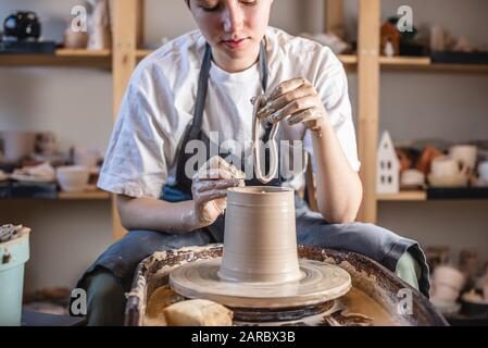 Potter che lavora su una ruota di Potter che fa un vaso. Giovane donna che forma l'argilla con le mani creando brocca in un laboratorio. Foto Stock