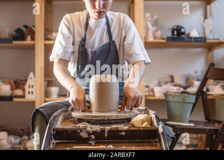 Donna vasaio che lavora su una ruota di Potter che fa un vaso. Master tira la brocca fuori dal cerchio bagnandola con acqua e tenendola delicatamente nelle mani Foto Stock