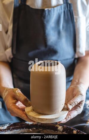 Donna vasaio che lavora su una ruota di Potter che fa un vaso. Master tira la brocca fuori dal cerchio bagnandola con acqua e tenendola delicatamente nelle mani. Clos Foto Stock