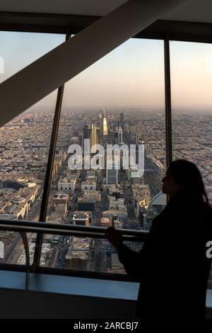 Viaggiatore straniero femminile in abaya nero che si affaccia sullo skyline di Riyadh in Arabia Saudita da un grattacielo nel centro della città durante il tramonto Foto Stock