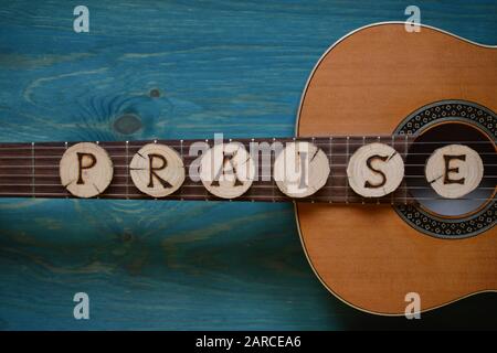 Chitarra su sfondo di legno teal con pezzi di legno su di esso scritta la parola: Lode Foto Stock