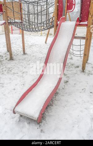 Scivolo per bambini coperto di neve durante le nevicate invernali in Cornovaglia. Metafora disturbi del tempo, scuola annullata, scuole chiuse. Foto Stock