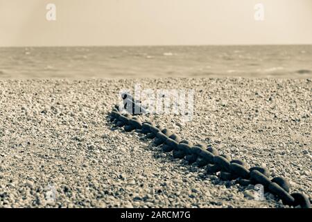 Rye Harbour Nature Reserve lunghezza vecchia catena arrugginita pesante sinistra sdraiata su spiaggia di pietra in tonalita' separate vecchio stile immagine. Foto Stock