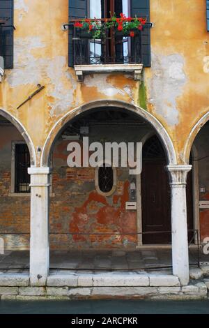 Un arco e una finestra con fiori di un tipico edificio si possono vedere su un canale di Venezia, in Italia Foto Stock