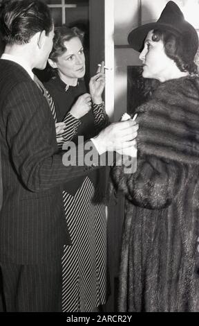 1940s, ospiti storici, adulti in conversazione a una festa di bevande presso una galleria d'arte di Londra, Londra, Inghilterra, Regno Unito, indossando le mode del giorno, con una signora in un cappotto e cappello di pelliccia di lusso. Foto Stock