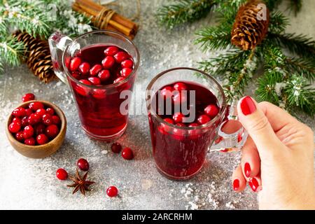 Bevande di Natale. Femmina tenuta a mano di bevanda calda invernale con mirtilli rossi e cannella su un tavolo di pietra chiaro. Foto Stock