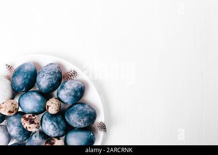 Bellissimo gruppo ombre blu uova di Pasqua con uova di quaglia e piume su uno sfondo di legno bianco. Concetto di Pasqua. Uova di confine. Copiare lo spazio per il testo. Colore blu classico dell'anno 2020 Foto Stock