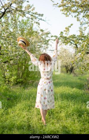 Giovane donna attraente con capelli ricci passeggiate nel verde di un giardino fiorito. La molla umore romantico. Foto Stock