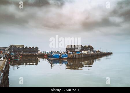 Due barche da pesca blu nel Whitstable Harbor, ormeggiate di fronte agli edifici nello stile di Fisherman Huts. Foto Stock