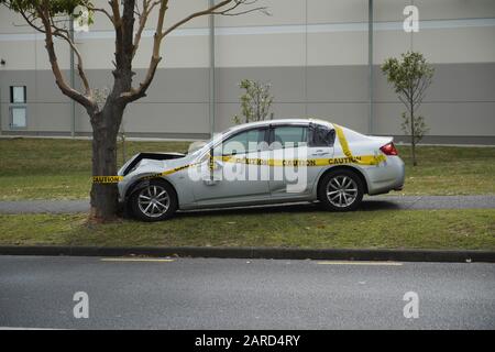 Silver Sedan auto montato marciapiede crash testa in albero giallo attenzione nastro di avvertimento avvolto intorno, Auckland, Nuova Zelanda. Foto Stock