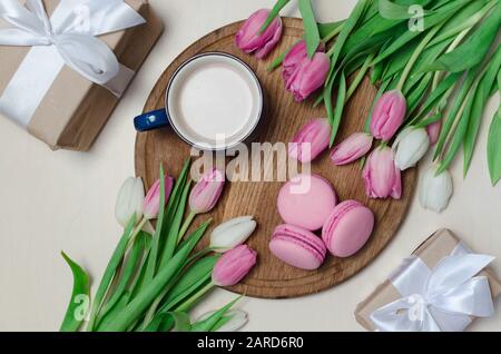 Tazza da caffè, fiori di tulipano primaverile e macaroni rosa su tavolo in legno vista dall'alto. Saluto per il giorno delle donne o delle madri Foto Stock