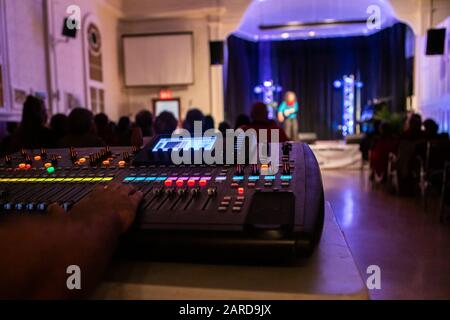 Immagine di closeup del mixer audio con controllo manuale ritagliato contro l'altoparlante femminile che dà voce in auditorium illuminato durante il festival Foto Stock