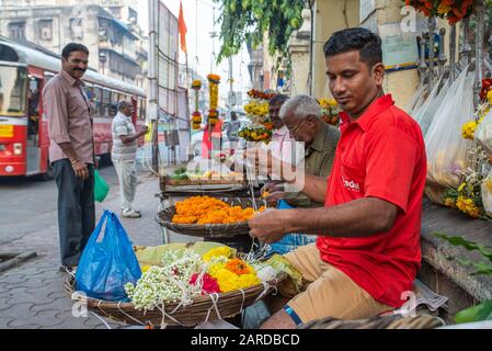 Mumbai, India - 17 dicembre 2017: I fornitori preparano collane marigvecchie di fronte a un passerby in una strada trafficata Foto Stock