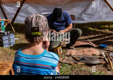 Vista posteriore del ragazzo in t-shirt blu con cappuccio e seduta su panca di legno. Contro l'uomo fare qualche opera d'arte sul prato in caso Foto Stock