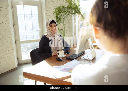 Revisione dei documenti con il collega. Bella donna d'affari arabo che indossa hijab mentre lavora in openspace o ufficio. Concetto di occupazione, libertà nell'area aziendale, leadership, successo, soluzione moderna. Foto Stock