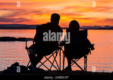 Una coppia siede e guarda il tramonto sull'Isola di Vancouver e sullo stretto di Haro come visto dal County Park sull'Isola di San Juan, Washington, USA. Foto Stock