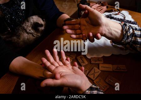 Una donna matura con un gatto sta intuendo le mani di un uomo sul palmo della sua mano.Chiudi le mani Foto Stock