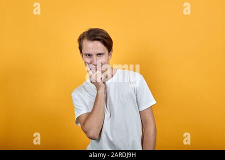 Lo sguardo snello del giovane uomo in t-shirt bianca, che tiene il mento in su con il dito indice Foto Stock
