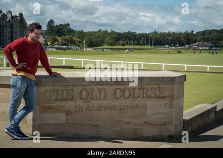 St Andrews, Regno Unito - 20 giugno 2019: Un bel turista maschio si appoggia sul segno al campo Vecchio al Royal e al Golf Club Antico di St. Andr Foto Stock