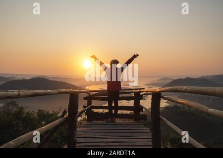 Una donna in piedi sul ponte di legno allegra mostra le mani durante l'alba Foto Stock