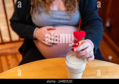 Una vista ad angolo elevato del fuoco selettivo di una donna gravida seduta al tavolo di legno godendo di un frullato organico sano con cannuccia di valentines di novità Foto Stock